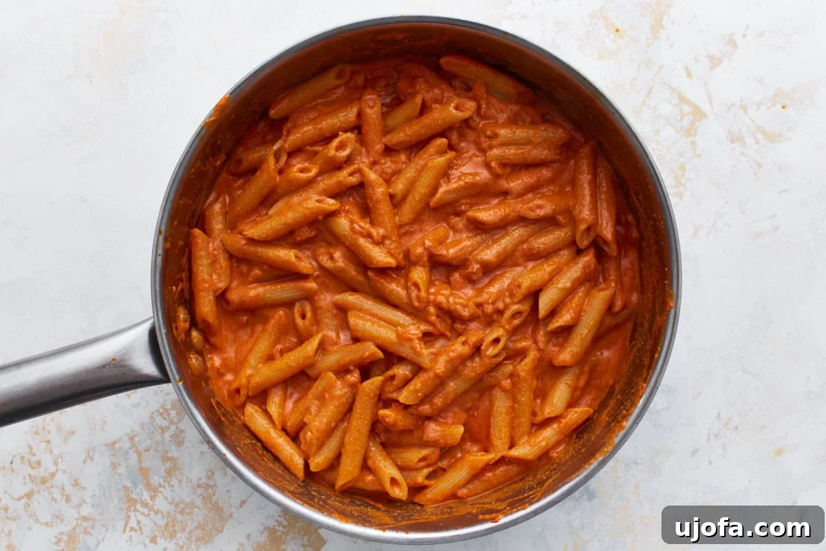 Gluten-free penne tossed into the creamy vegan vodka sauce in the skillet.