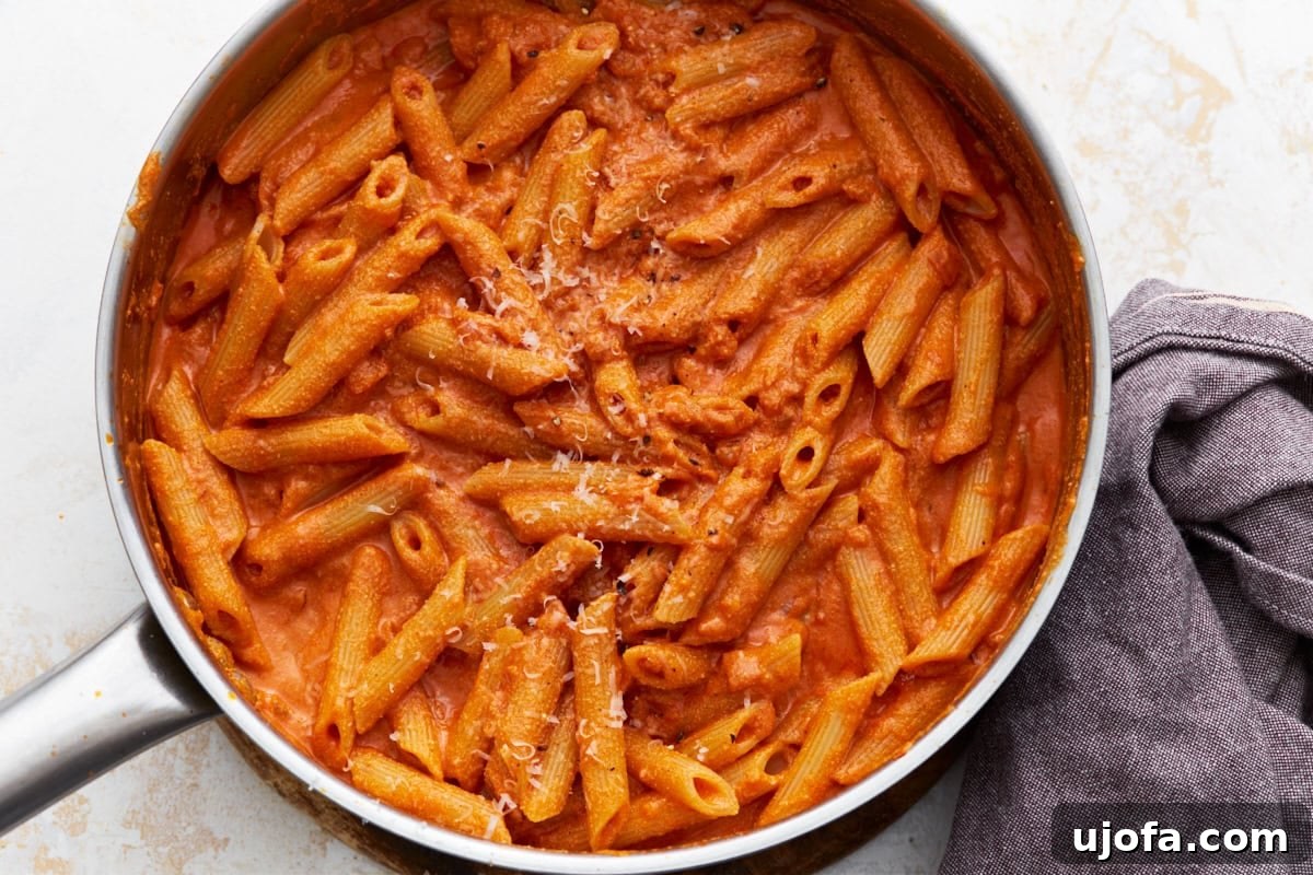 Finished vegan vodka pasta in a skillet, garnished with vegan parmesan, with a cloth napkin on the side.