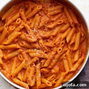 A pan filled with gluten-free penne pasta coated in creamy vegan vodka sauce, sprinkled lightly with vegan parmesan.