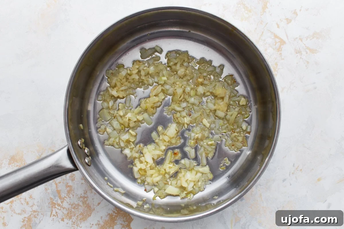 Chopped onions and garlic sautéing in olive oil in a stainless steel skillet until softened.