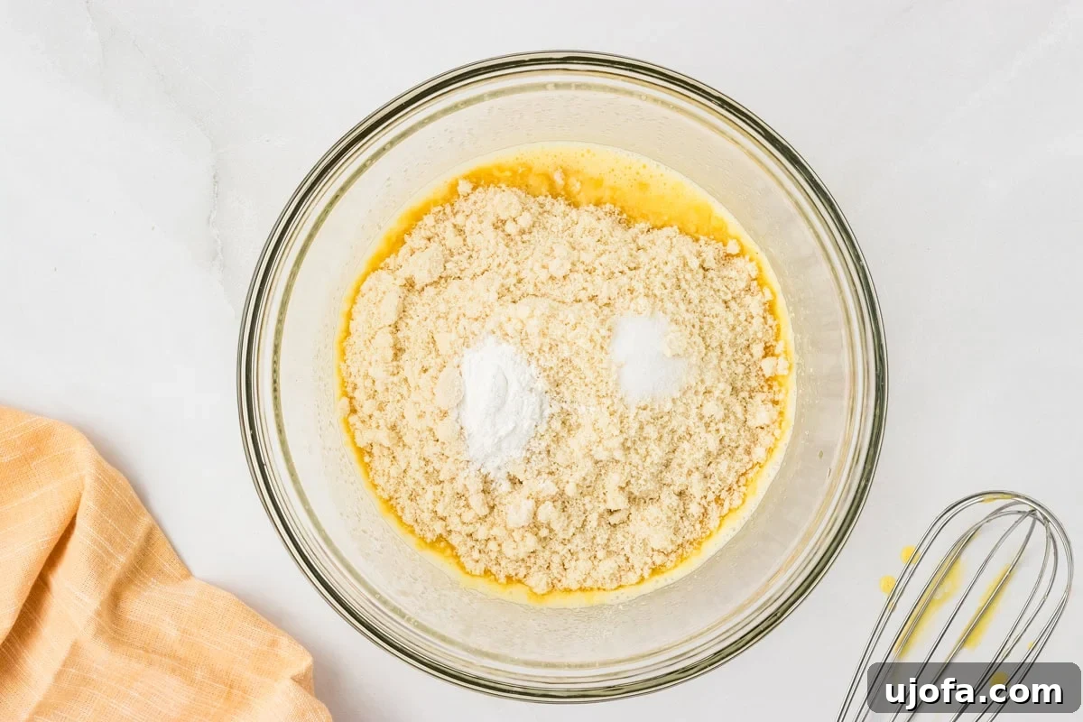 Guilt-Free Golden Cornbread 5 Bowl of wet ingredients topped with almond flour, baking powder, and salt before mixing, ready to combine the dry and wet components for the cornbread batter.