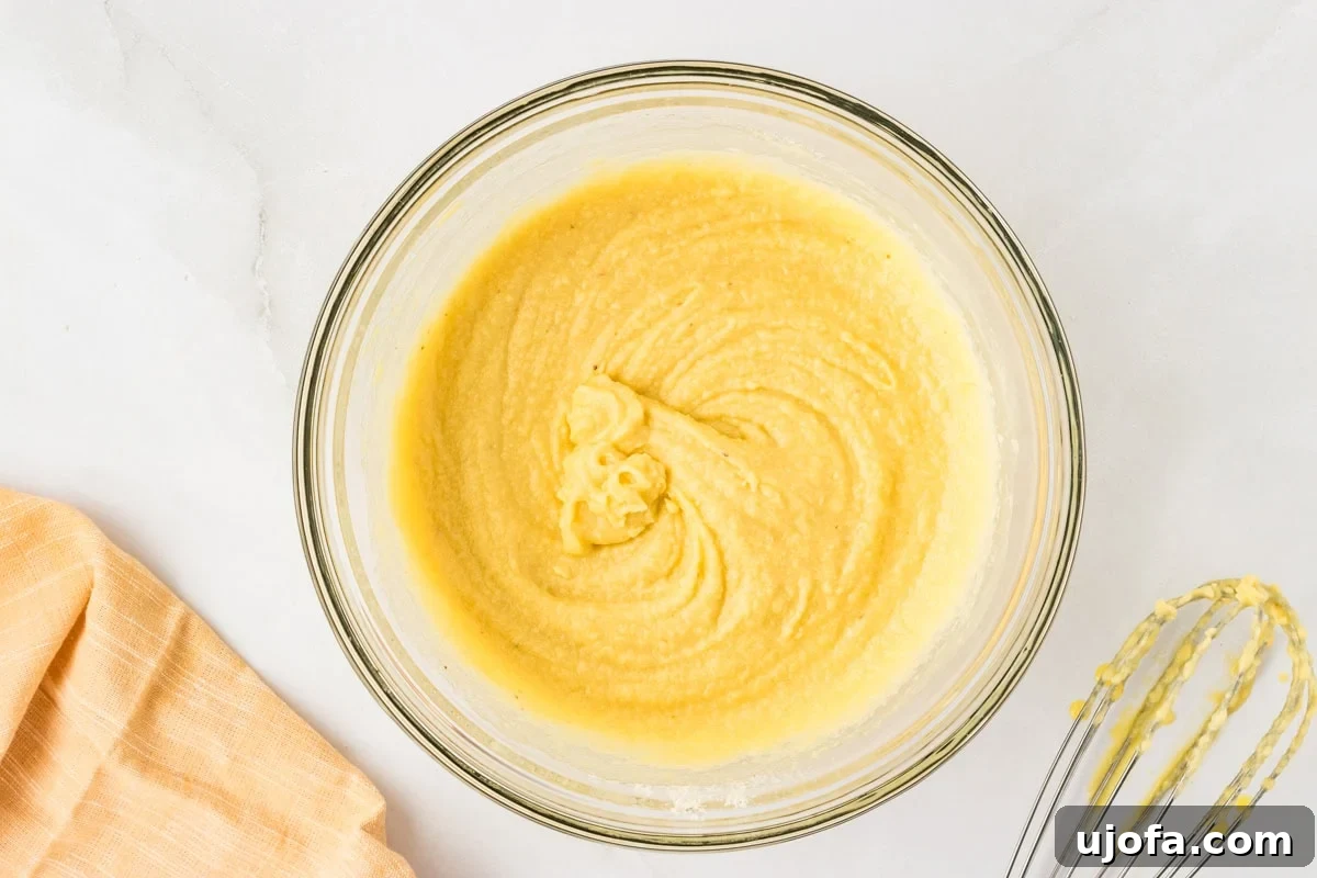 Guilt-Free Golden Cornbread 6 Smooth yellow cornbread batter in a glass bowl after mixing, with a whisk resting nearby, showing the perfect consistency before pouring into the baking dish.