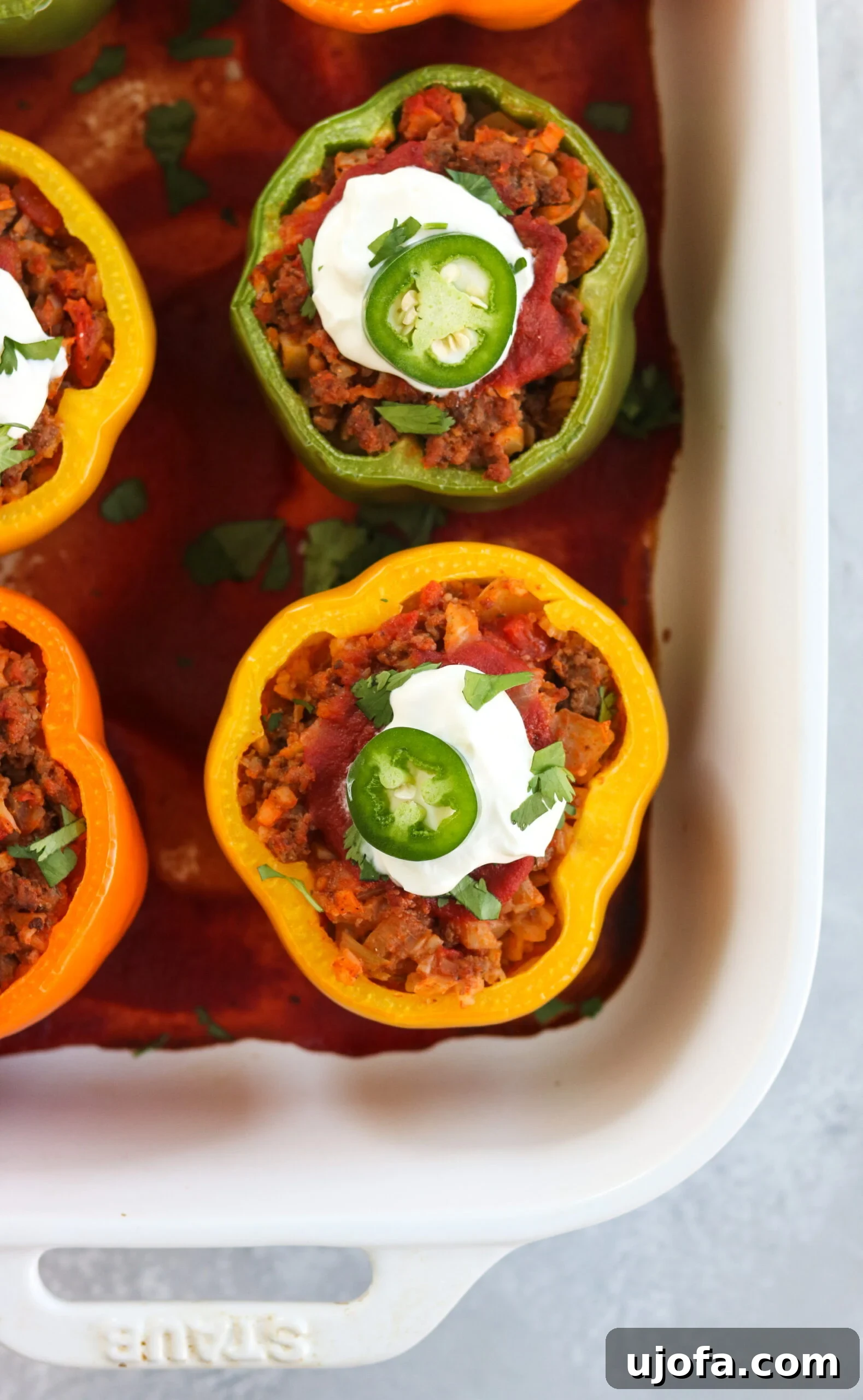 Two vibrant red bell peppers stuffed with a savory taco filling and topped with fresh cilantro, ready to be served on a white plate.