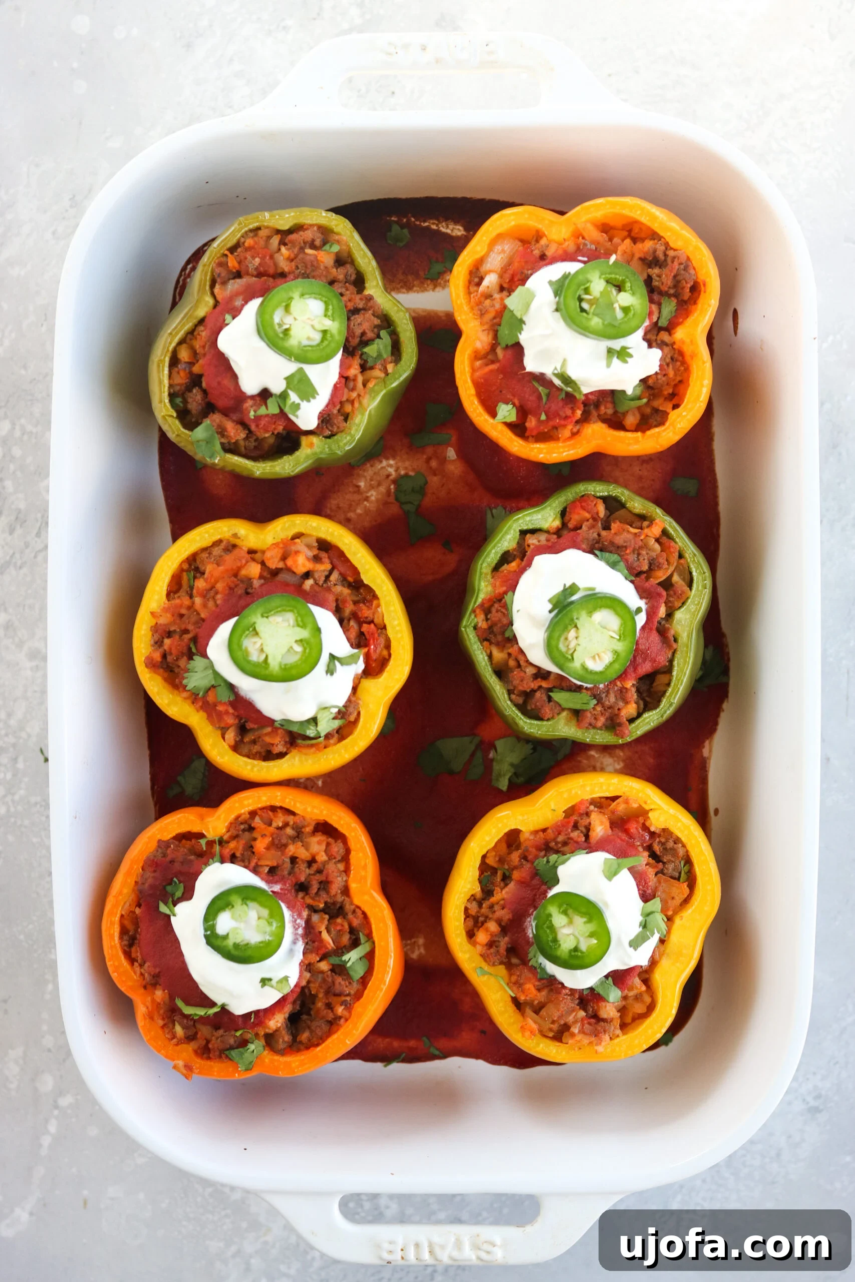 A close-up of a rustic wooden cutting board showcasing a beautifully arranged Whole30 Taco Stuffed Pepper next to fresh cilantro and lime wedges.