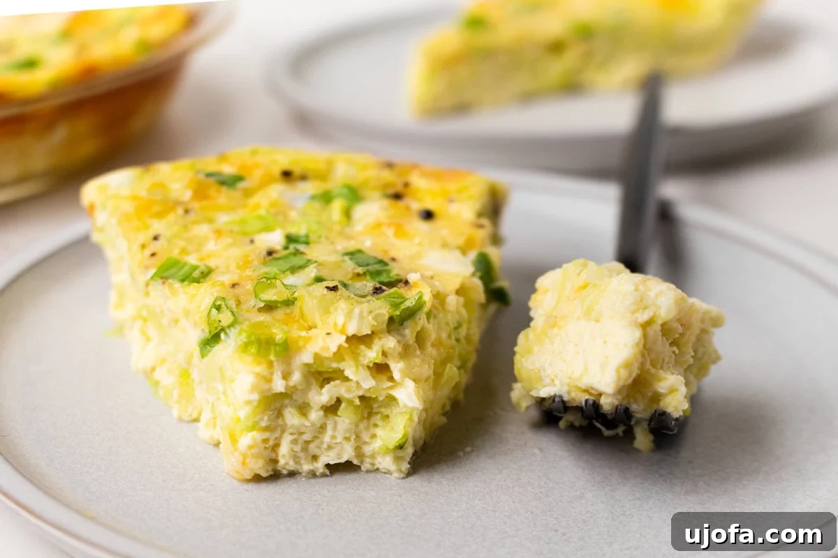 Fluffy Zucchini Egg Bake 12 An inviting slice of crustless zucchini quiche presented on a clean white plate, with a fork holding a bite that reveals the fluffy, cheesy, and tender zucchini-filled texture, ready to be enjoyed.
