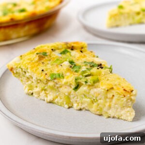 A slice of crustless zucchini quiche on a gray plate, topped with green onions, with the full quiche visible in the background.