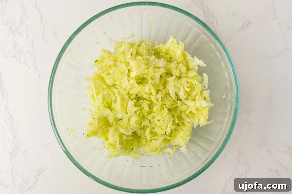 Fluffy Zucchini Egg Bake 5 Freshly shredded zucchini piled high in a clear glass mixing bowl, ready for the next step of moisture removal, resting on a clean marble countertop.