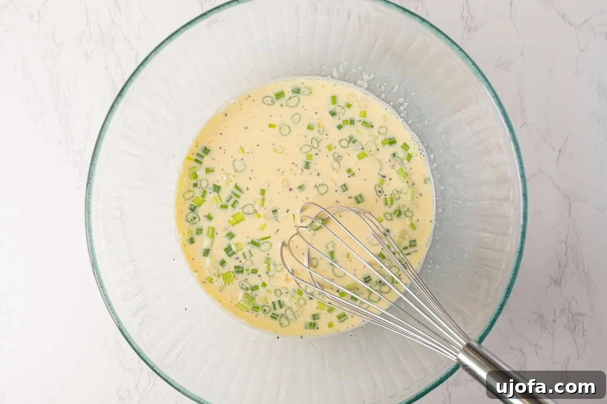 Fluffy Zucchini Egg Bake 7 A vibrant bowl containing the quiche egg mixture, featuring finely chopped green onions, a creamy texture from half and half, and a blend of salt, pepper, and garlic powder, all whisked together.