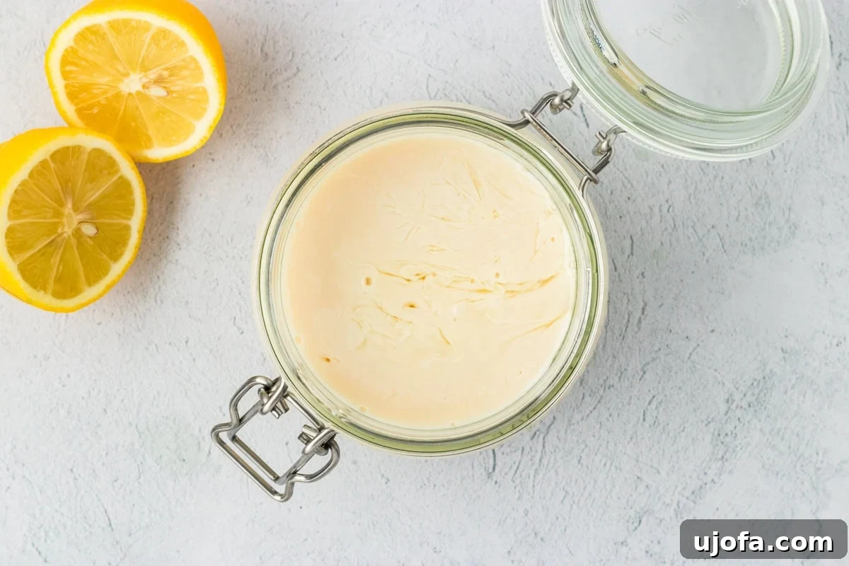 A glass jar filled with freshly curdled vegan buttermilk on a light countertop with halved lemons beside it.