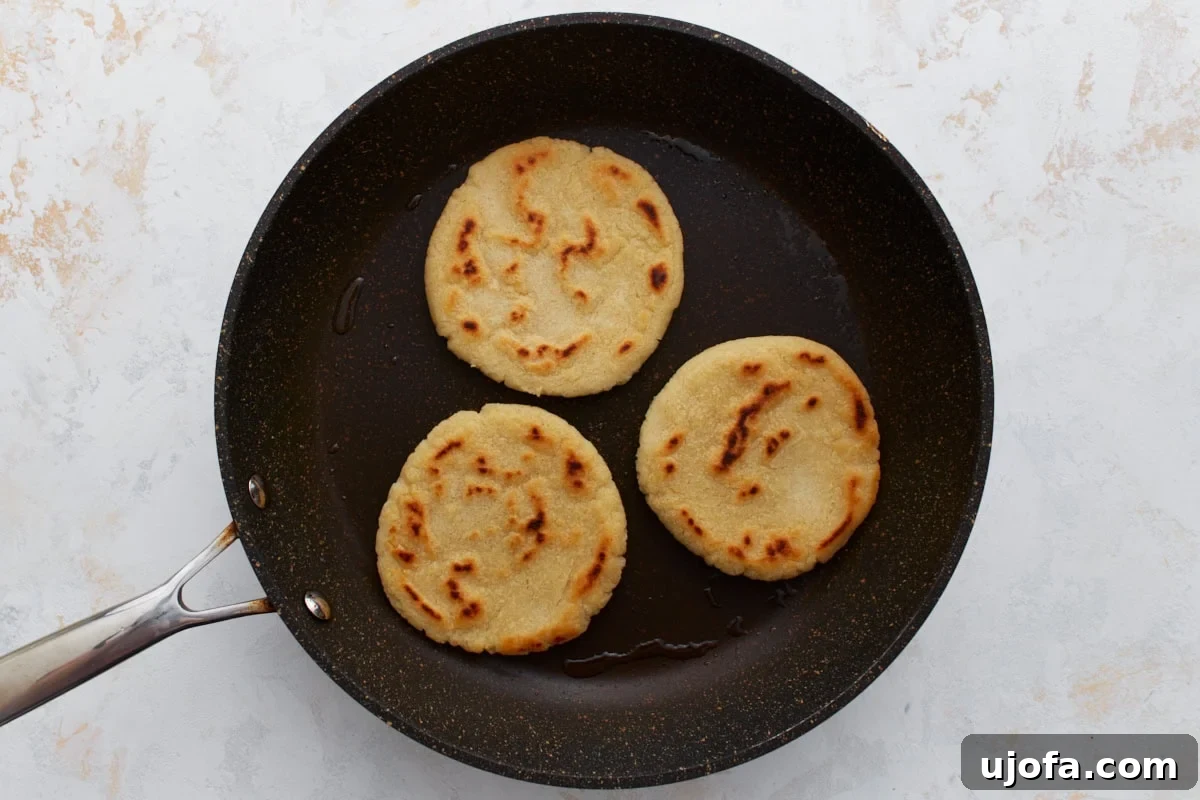 Authentic Mexican Gorditas 9 Three gluten-free gorditas actively cooking in a skillet, displaying golden brown spots and a slight puff, indicating they are almost done.