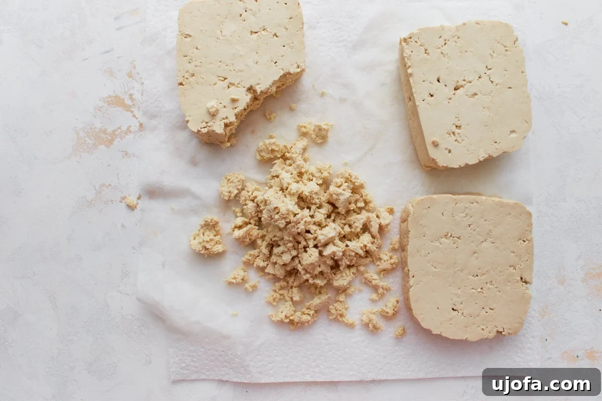 Vegan Farmhouse Curds 5 Blocks of firm tofu on a white paper towel, with some pieces crumbled into small, cottage cheese–like curds, ready for the next step.