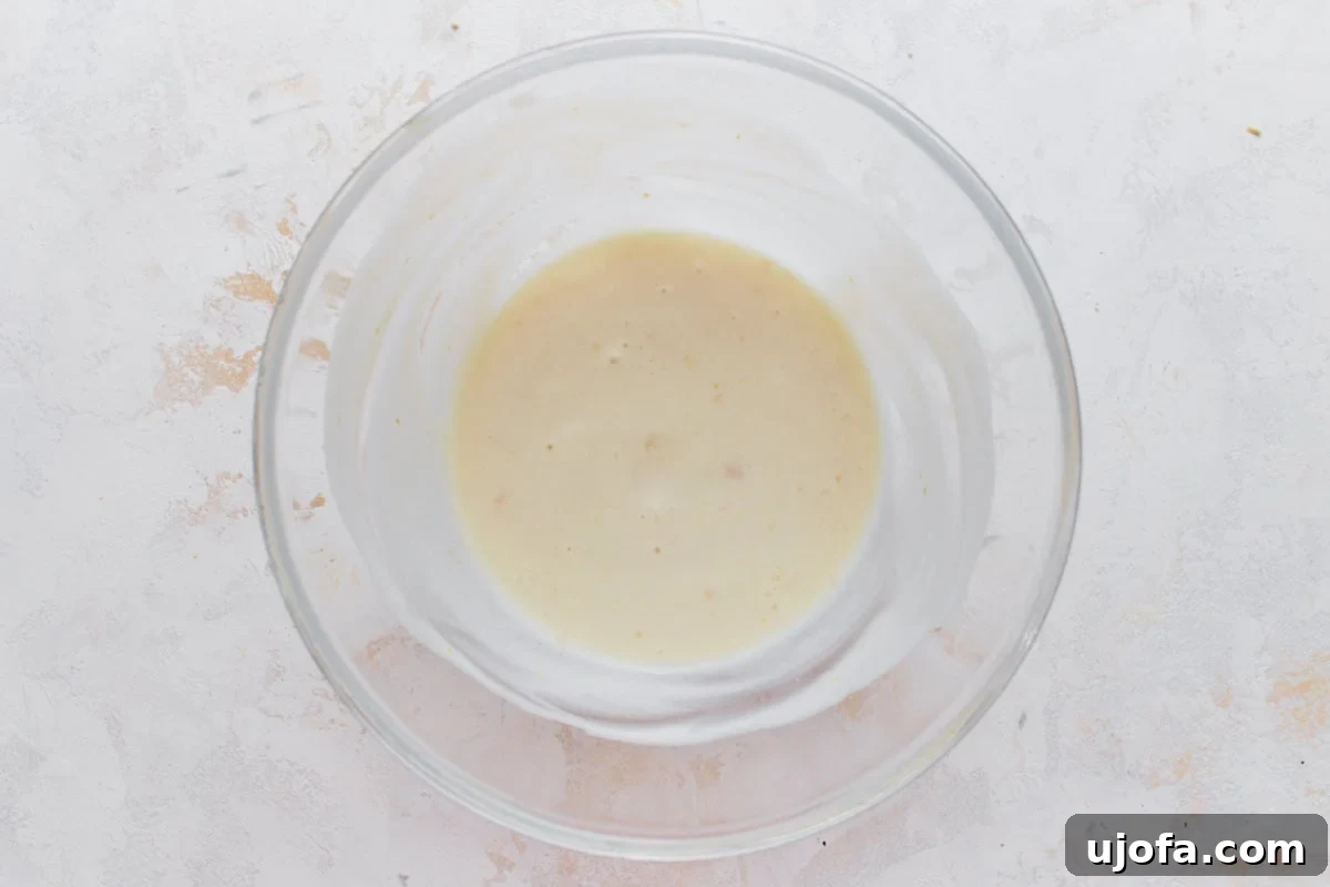 Vegan Farmhouse Curds 6 A glass mixing bowl containing a smooth, pale yellow yogurt and lemon mixture, showing the creamy base for the dairy-free cottage cheese dressing.
