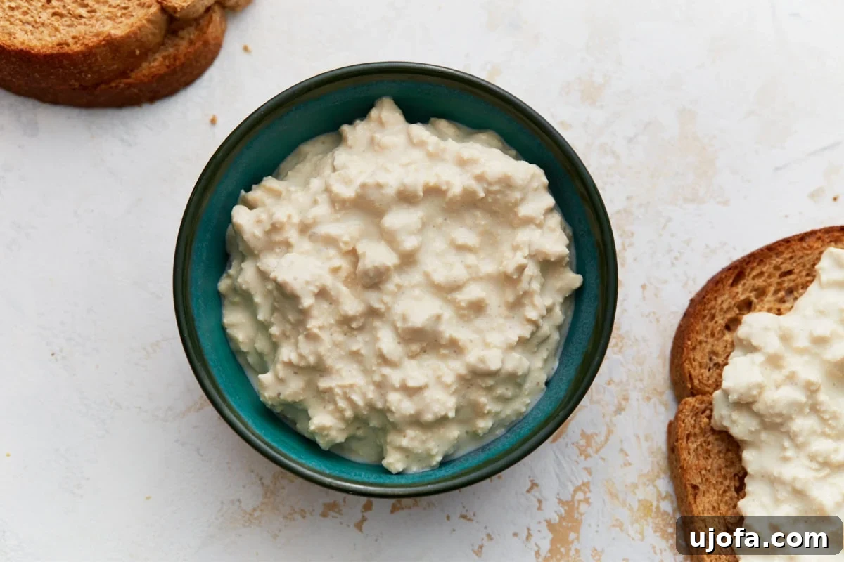 Vegan Farmhouse Curds 8 A teal bowl of finished dairy-free cottage cheese, perfectly chilled and ready to eat, placed next to slices of toasted bread on a light surface.