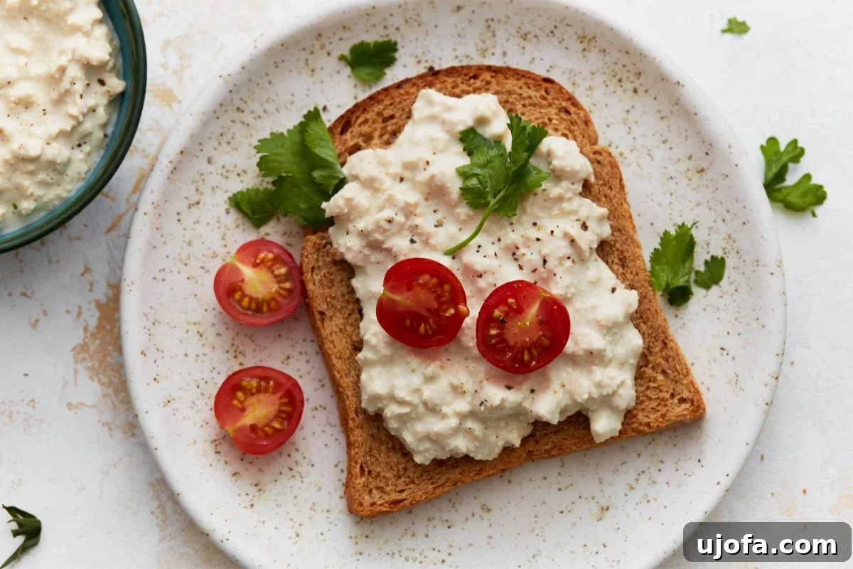 Vegan Farmhouse Curds 9 A slice of toast generously topped with dairy-free cottage cheese, vibrant cherry tomato halves, and fresh parsley, presented on a white plate, showcasing a delicious serving suggestion.