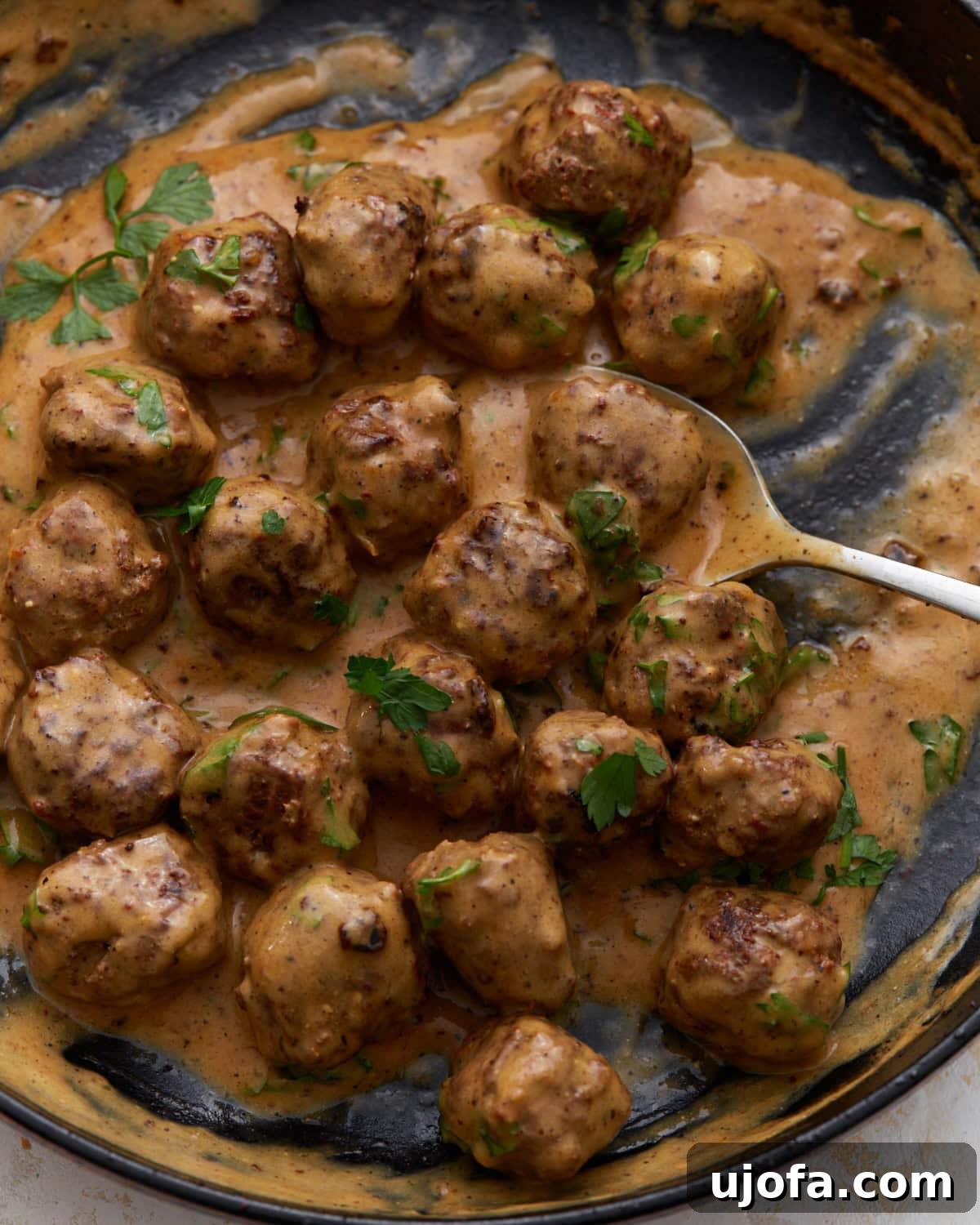 Keto Swedish meatballs in a creamy sauce garnished with fresh parsley in a cast-iron skillet, showcasing a delectable low-carb comfort meal.
