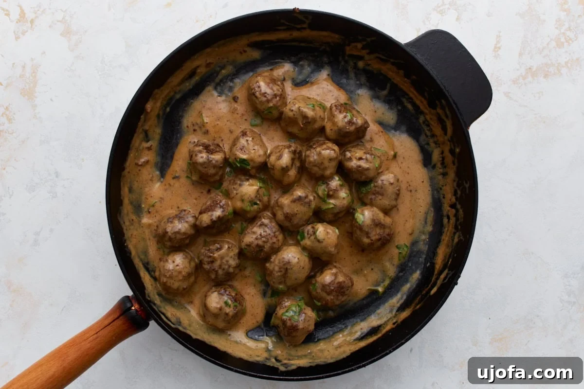 Cooked Swedish meatballs bathed in creamy sauce, beautifully garnished with fresh parsley in a skillet, signaling the dish is ready to be served.