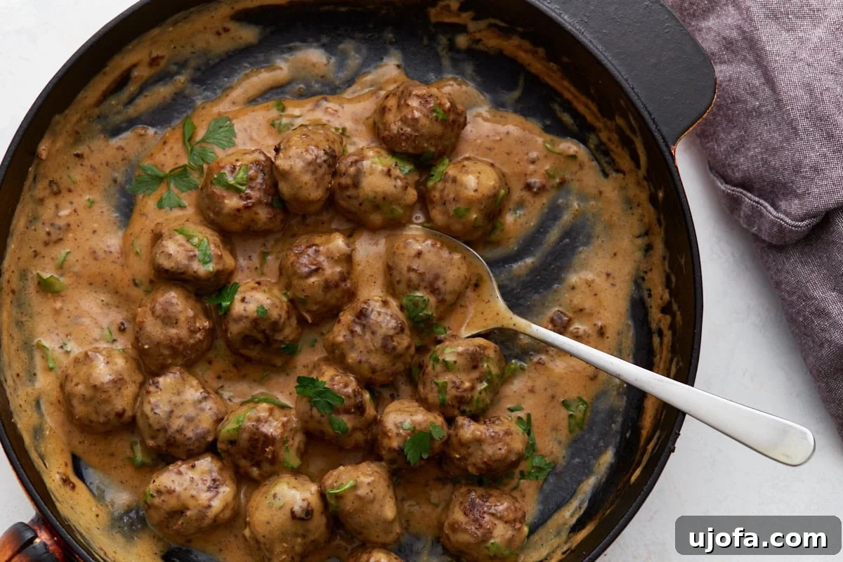 A generous serving of Keto Swedish meatballs, coated in creamy sauce with parsley, resting in a skillet alongside a serving spoon, inviting you to dig in.