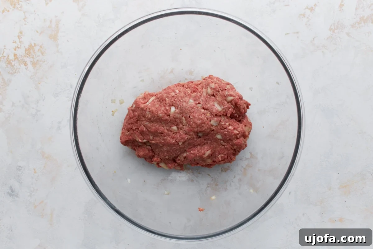 The ground meat mixture, combined with finely diced onions, almond flour, egg, and a blend of aromatic spices, resting in a glass bowl, ready to be formed into meatballs.