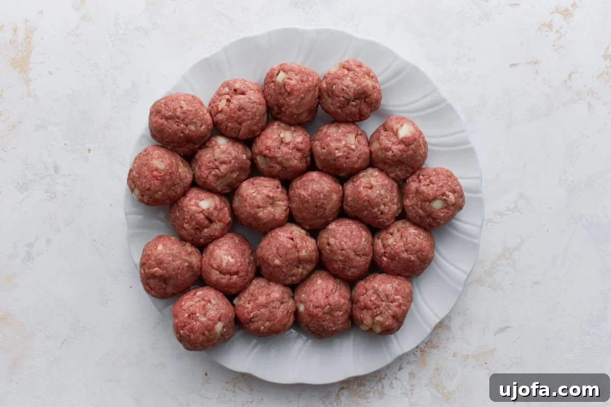 Approximately 24 uncooked Swedish meatballs, uniformly rolled and neatly arranged on a white plate, patiently awaiting their turn in the skillet.