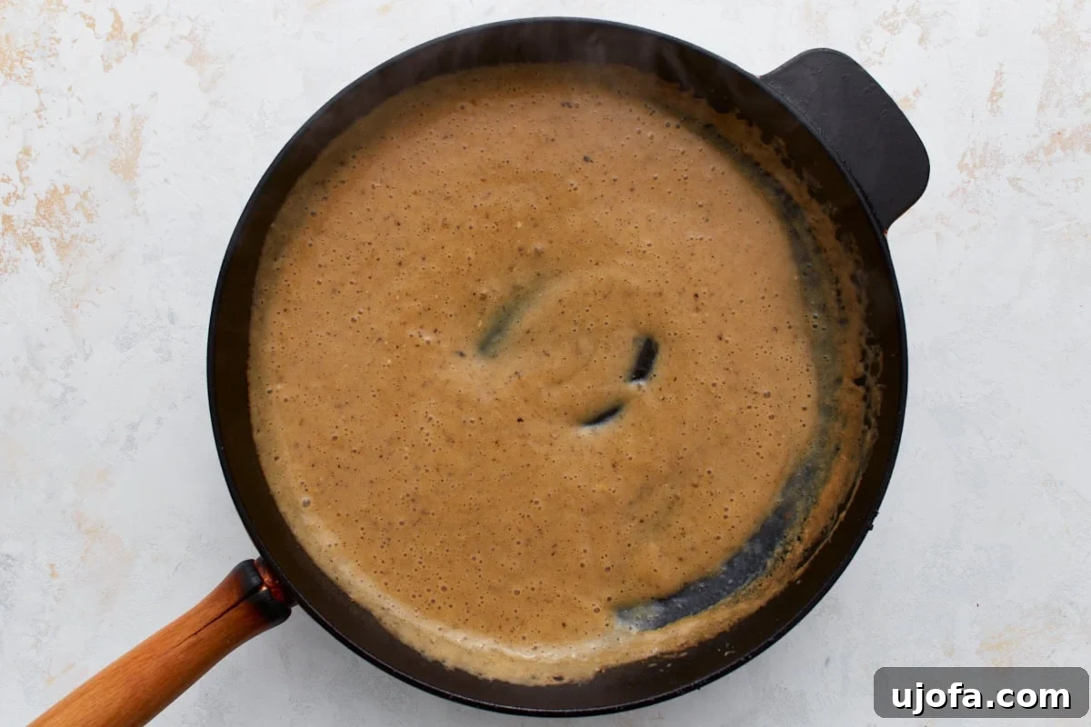 The creamy Swedish meatball sauce, rich and smooth, simmering gently in the skillet, indicating it's reaching the perfect thickened consistency.