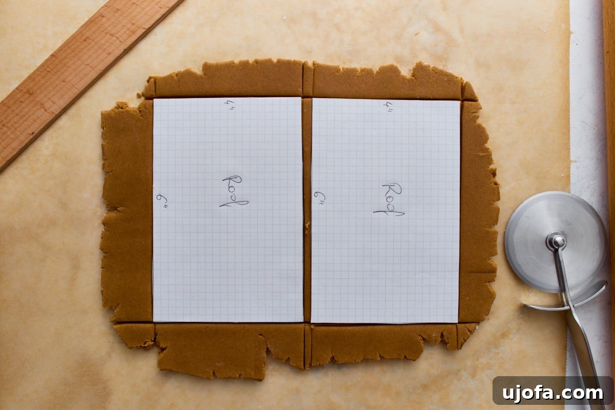 A piece of rolled gingerbread dough with graph-paper roof templates placed on top, ready to be trimmed with a pizza cutter.