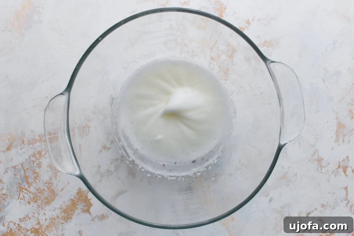 A glass bowl with glossy white egg whites beaten until soft peaks form, the start of making royal icing.