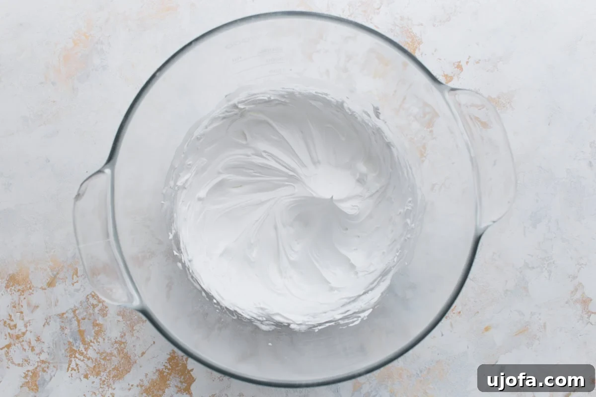 A glass mixing bowl filled with thick, smooth white royal icing whipped to stiff peaks, ready for piping.