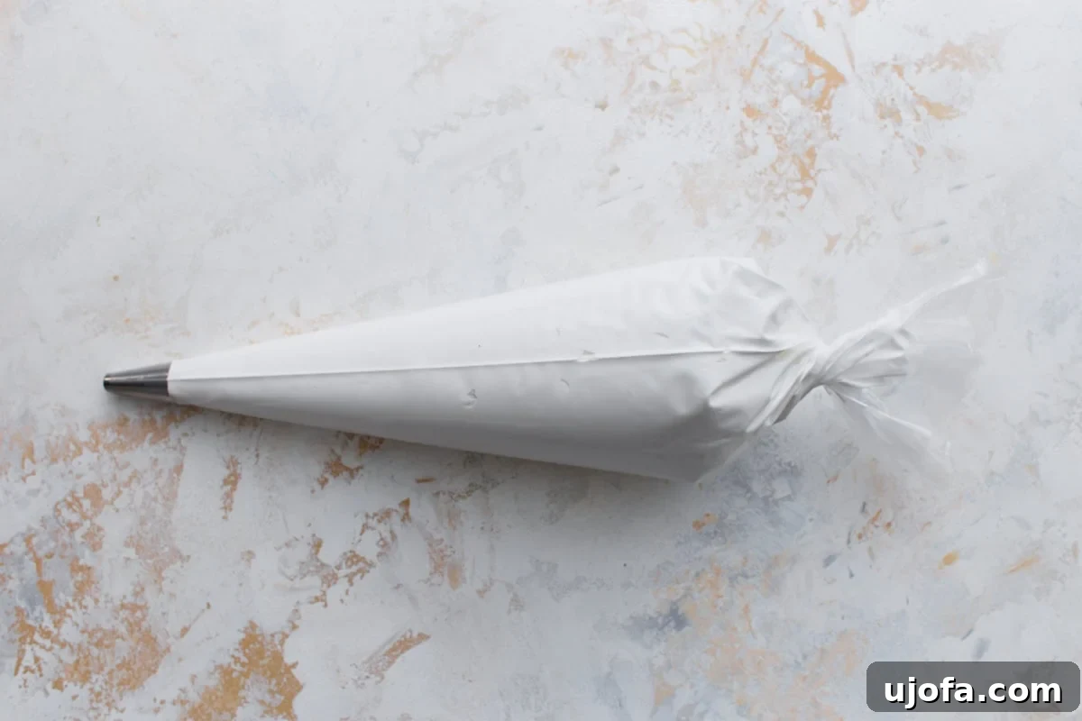 A large piping bag filled with white royal icing and fitted with a metal tip, resting on a light background.