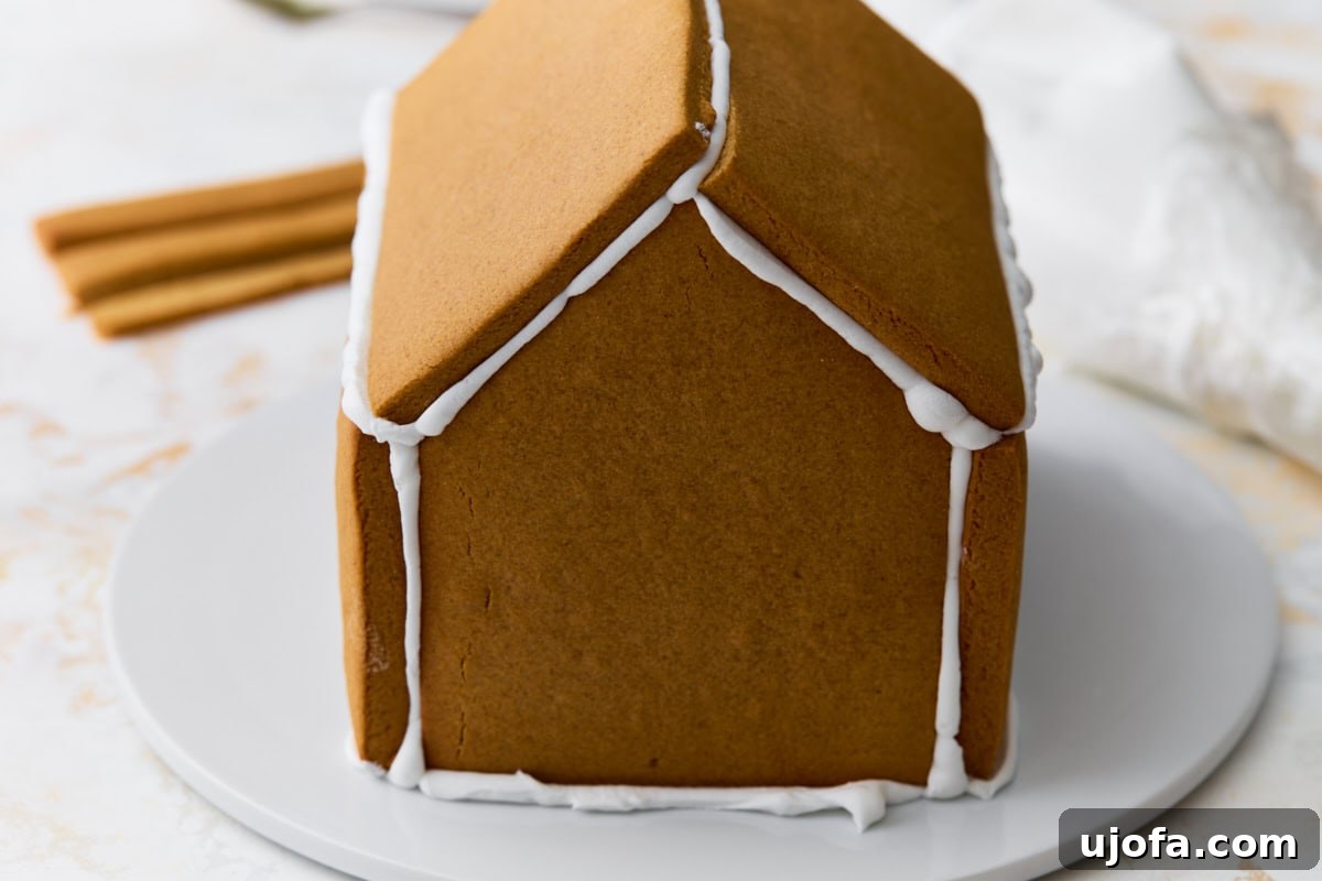 The gingerbread house partially assembled with roof panels attached and seams sealed with white royal icing.