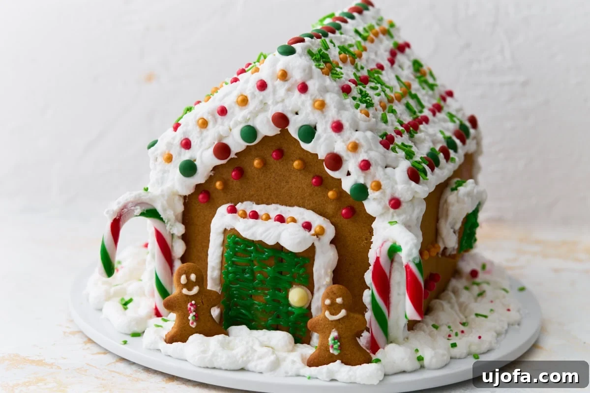 A fully decorated gluten-free gingerbread house with candy canes, colorful candies, and piped white icing viewed from a side angle.