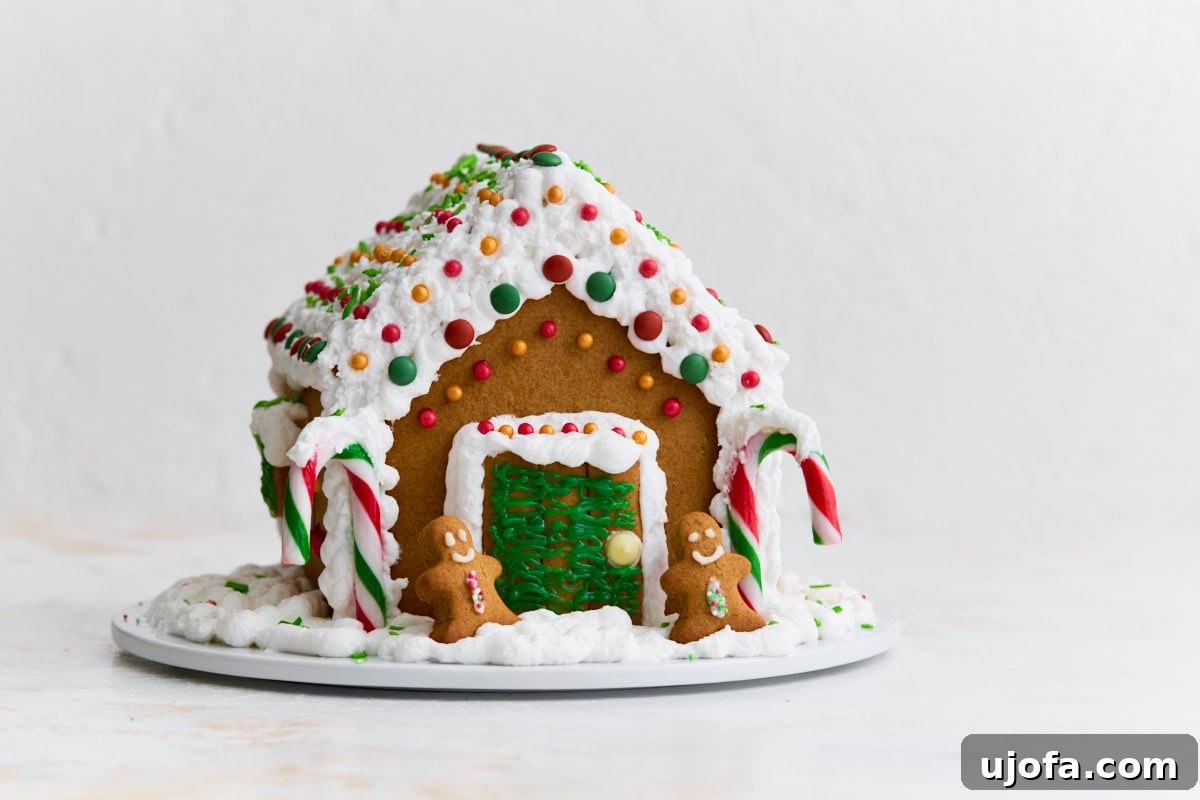 The completed gluten-free gingerbread house shown from the front, with candy canes framing the door and two small gingerbread people in front.