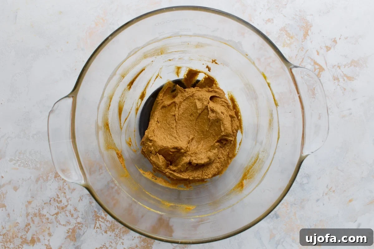 A glass mixing bowl with creamed butter, brown sugar, and molasses forming a fluffy golden base for the gingerbread dough.