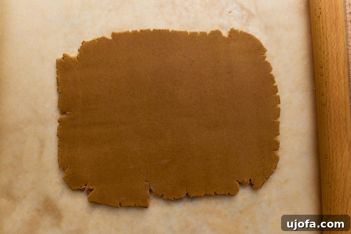 A sheet of rolled-out gingerbread dough between parchment paper, about ¼ inch thick, ready for cutting house templates.