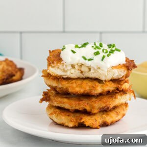 Stack of crispy gluten-free potato latkes topped with sour cream and chopped chives on a white plate, showcasing their perfect golden-brown texture.