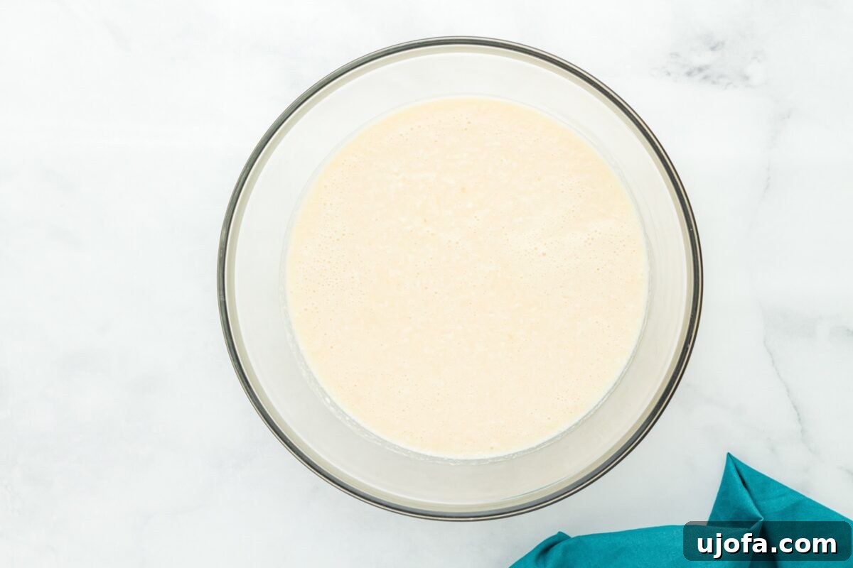 Velvet Coconut Dream 8 A clear glass mixing bowl holds a creamy pie batter, now thoroughly mixed with white shredded coconut, creating a textured and inviting mixture, prepared to be poured.