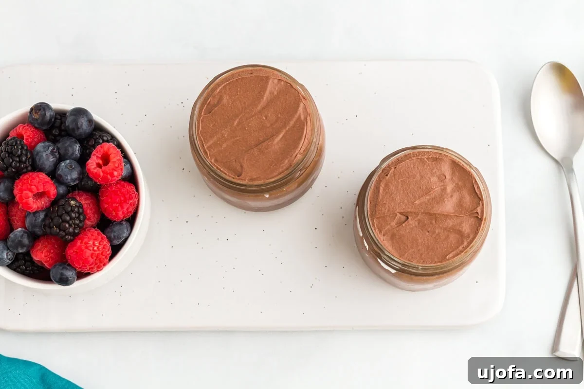 Decadent Vegan Chocolate Treat 8 Two small jars filled with vegan chocolate mousse set on a white tray next to a bowl of fresh raspberries, blueberries, and blackberries.
