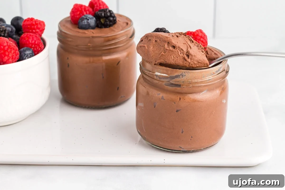 Decadent Vegan Chocolate Treat 9 Two jars of vegan chocolate mousse topped with fresh berries, with a spoonful of mousse lifted from one jar and a bowl of mixed berries beside them.