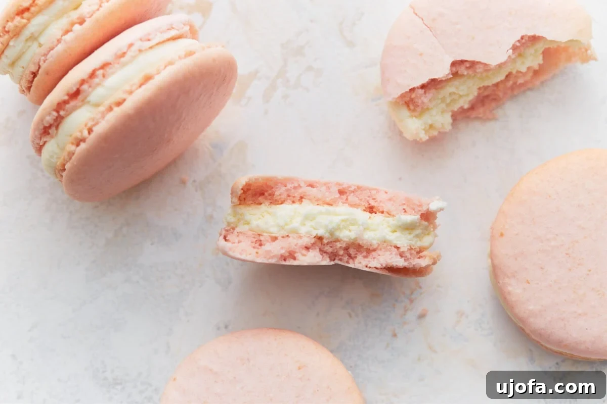 A close-up of several macaron halves, revealing the crisp outer shell and the smooth, rich buttercream center. Whole macarons are arranged around them, showcasing the variety and perfect texture.