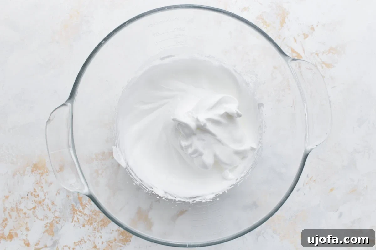 Stiff, glossy egg white meringue whipped to perfection in a clear glass mixing bowl, showcasing its firm texture.