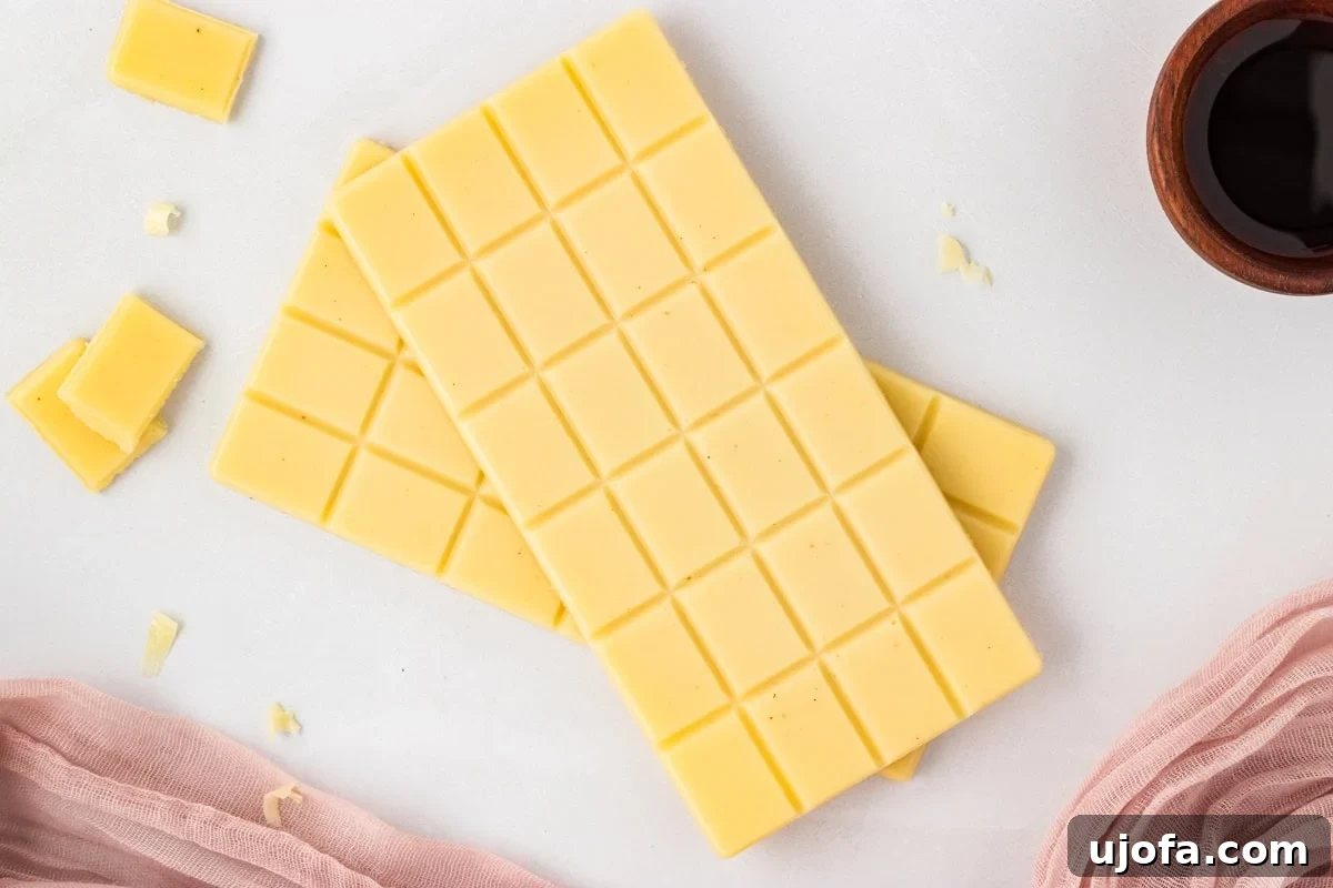 Two finished vegan white chocolate bars on a white surface with small broken pieces nearby.