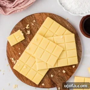 Vegan white chocolate bars stacked on a wooden board with small shaved pieces scattered around.