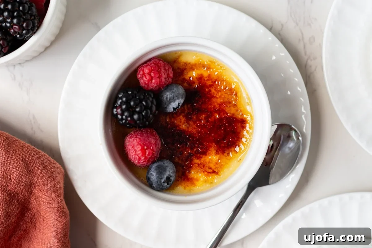 Plant Based Crème Brûlée Bliss 12 A dairy-free crème brûlée perfectly set in a white ramekin, adorned with fresh berries, showcasing its crisp caramelized topping ready to be cracked.