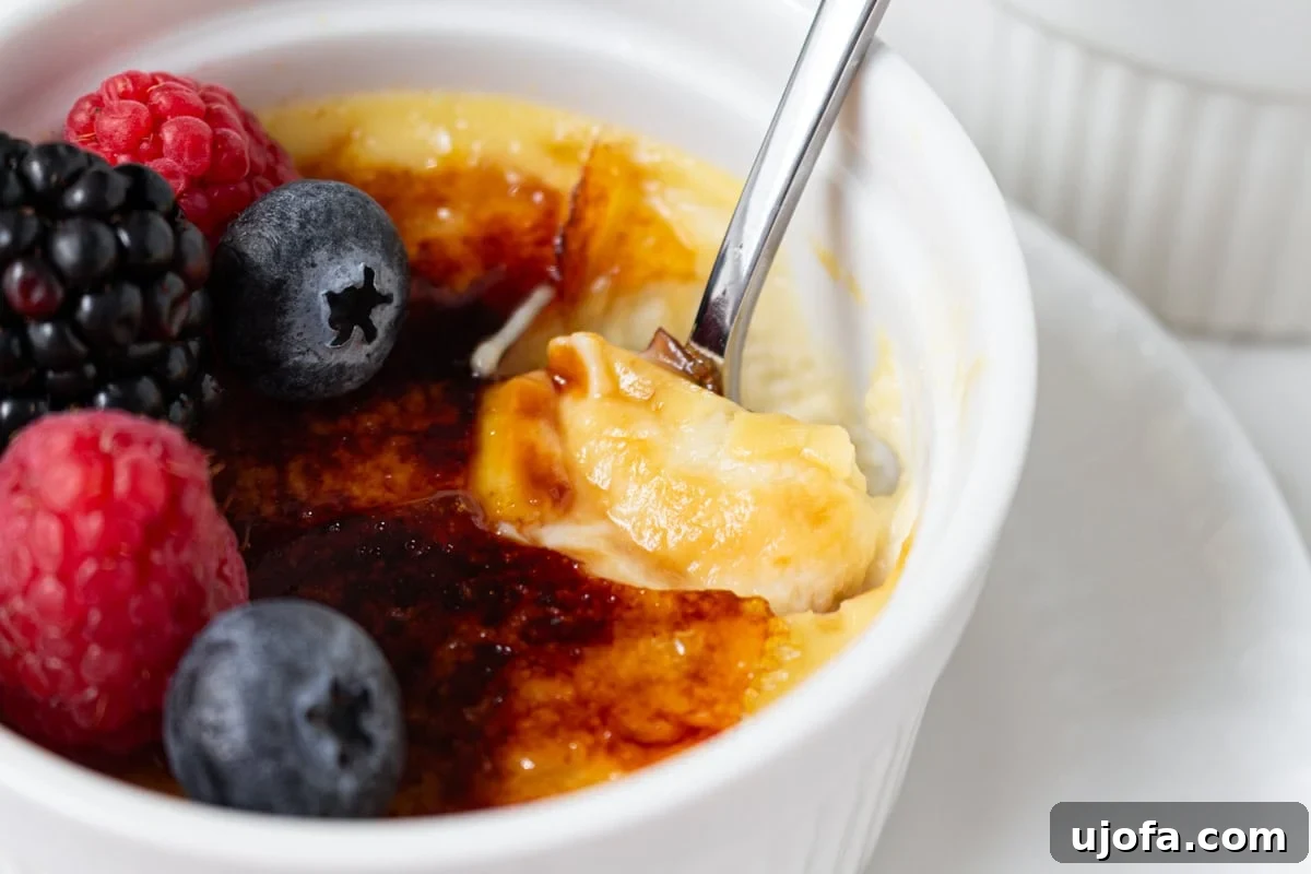 Plant Based Crème Brûlée Bliss 13 A spoon breaking through the crackly caramelized sugar top of a dairy-free crème brûlée, revealing the smooth custard beneath.