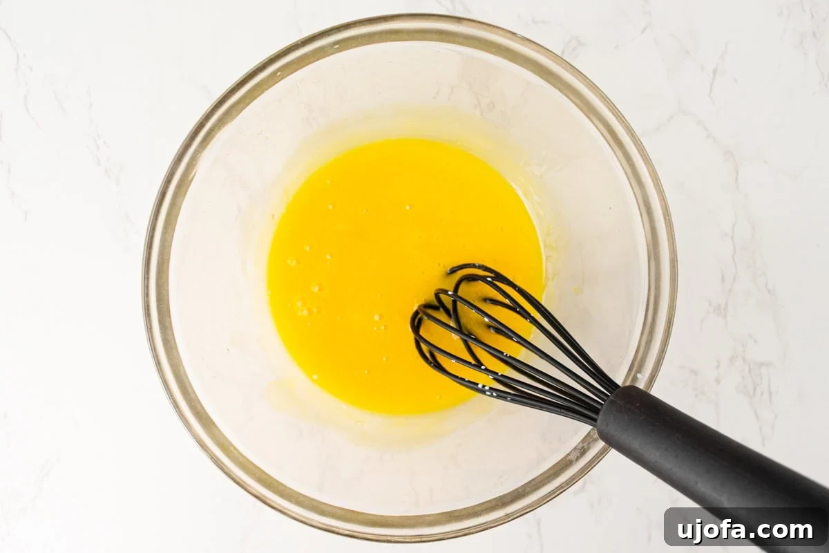 Plant Based Crème Brûlée Bliss 7 Five bright yellow egg yolks being briskly whisked in a clear glass bowl, creating a smooth, airy consistency.