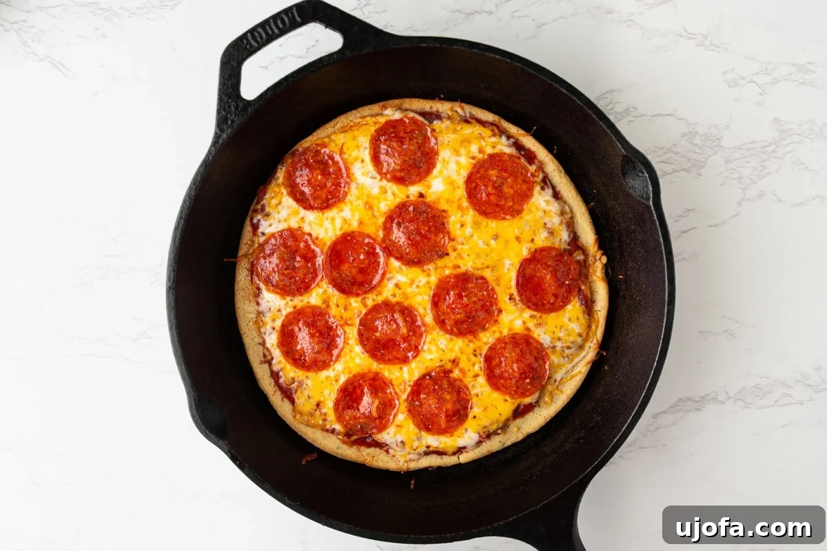 Baked chickpea pizza crust with melted cheese and pepperoni in a cast iron pan