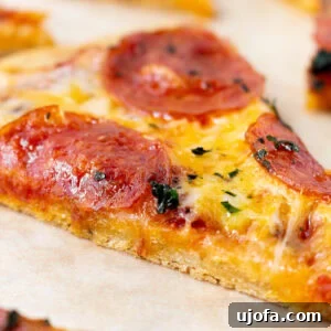 Slice of chickpea pizza crust topped with melted cheese and pepperoni on parchment paper