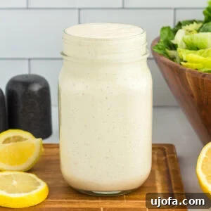 Mason jar of dairy-free Caesar dressing on a wooden board with lemon slices and romaine lettuce in the background