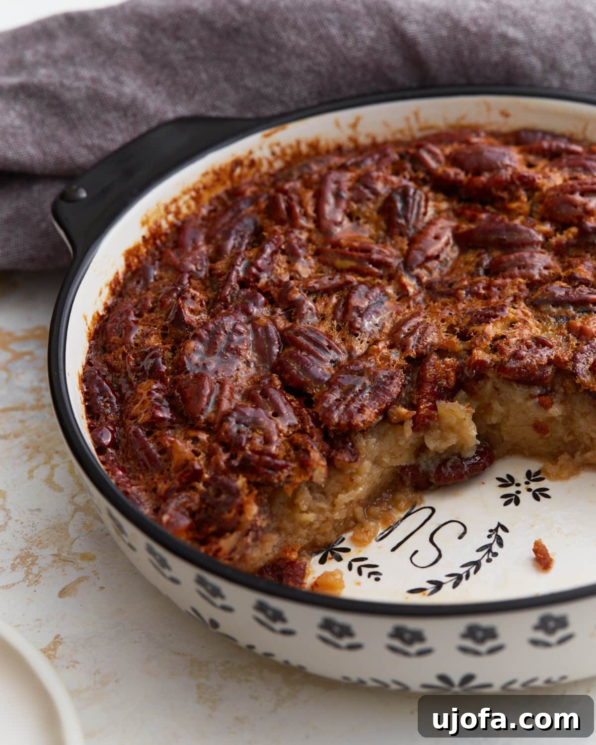 Crust Free Pecan Perfection 2 A beautifully baked crustless pecan pie in a ceramic dish, with one slice removed to reveal its luscious, gooey filling packed with pecans.