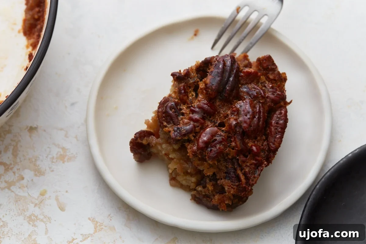 Crust Free Pecan Perfection 10 A close-up of a slice of crustless pecan pie on a white plate, with a fork gently touching the gooey, pecan-filled center.