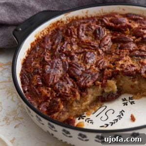 Crustless pecan pie baked in a ceramic pie dish with a slice removed, showing the gooey pecan filling